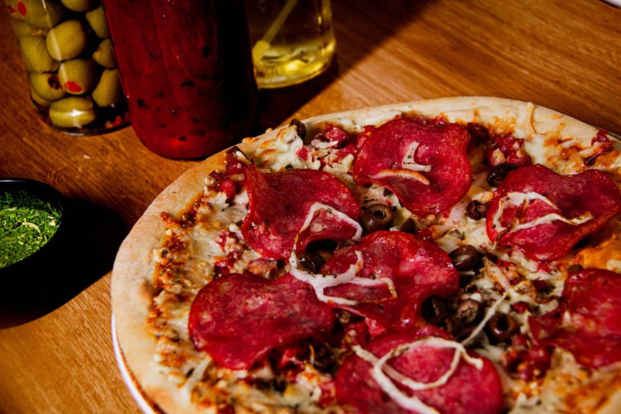 Pizza artesanal de calabresa, still com ingredientes ao fundo